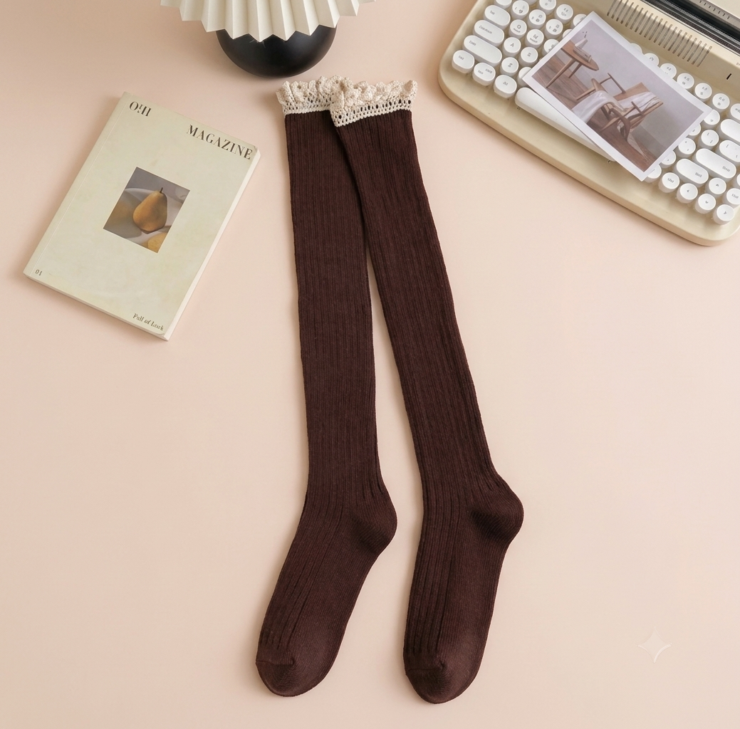 Over the knee boot socks in dark brown, featuring a ribbed thigh-high length. Styled flat beside a book and keyboard.
