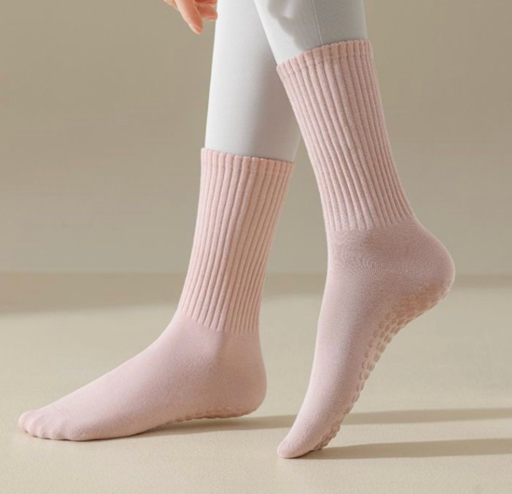 Pilates crew socks in pink ribbed knit, featuring a non-slip grip sole. Worn on the feet during practice.