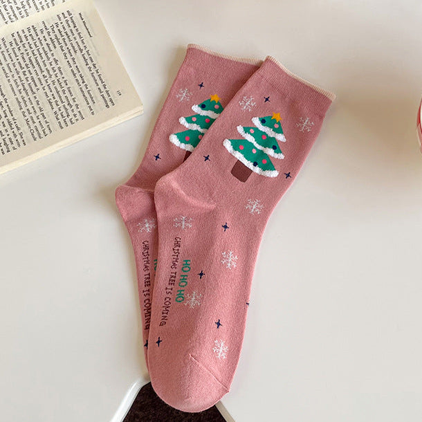Pink Christmas socks with a Christmas-tree design, flat-lay pair beside an open book.