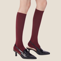 Red high knee socks in burgundy ribbed knit, featuring a navy accent cuff. Worn on legs with heels.