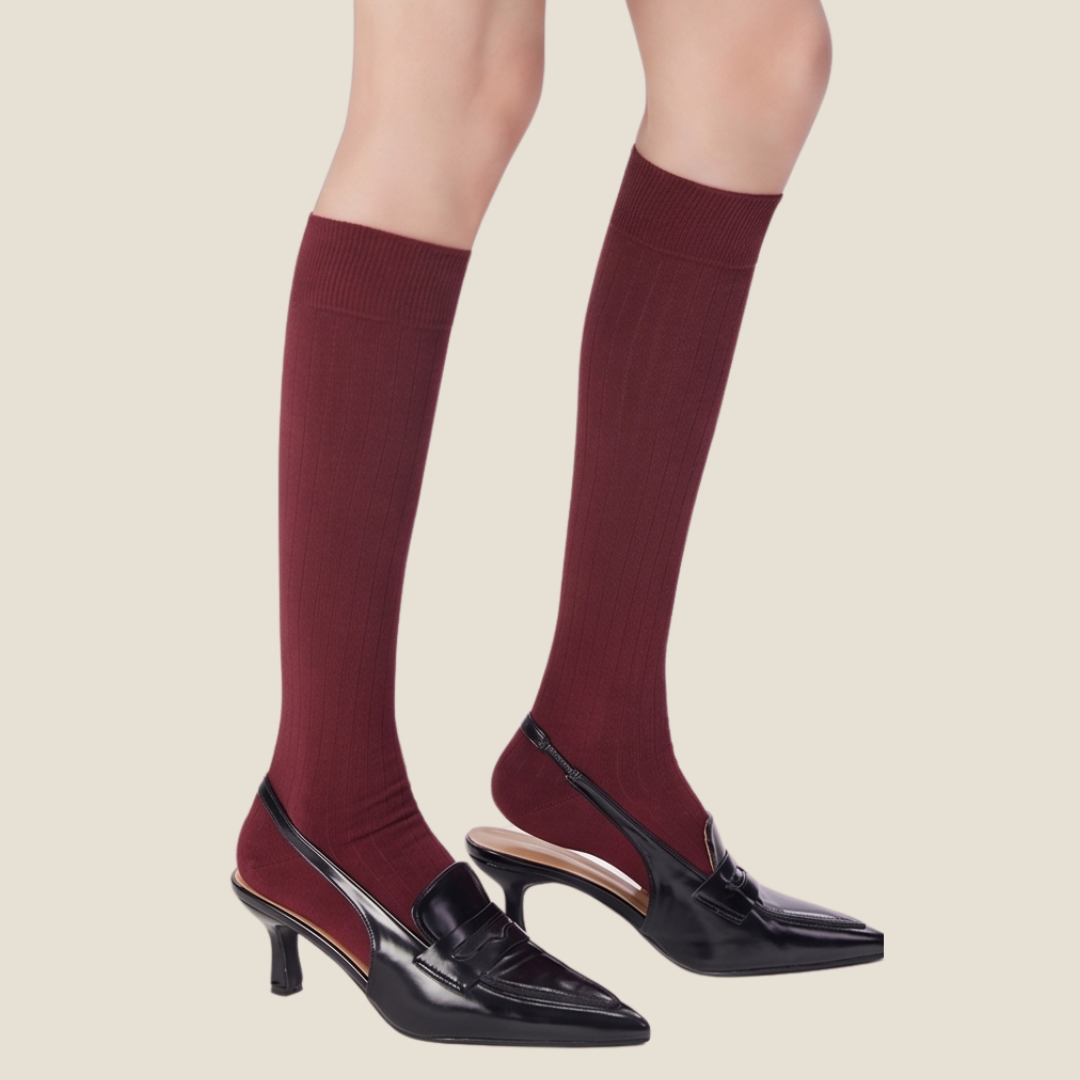 Red high knee socks in burgundy ribbed knit, featuring a navy accent cuff. Worn on legs with heels.