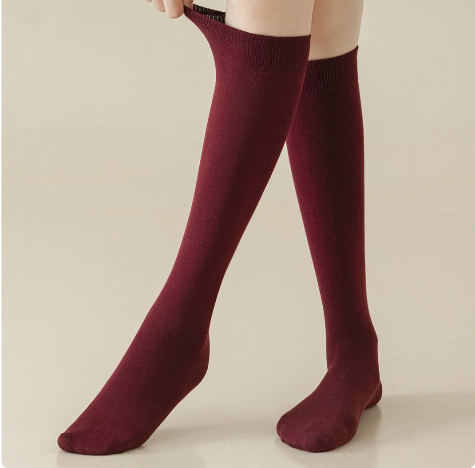 Red knee socks in burgundy ribbed knit, featuring a smooth knee-high leg. Worn on legs against a warm backdrop.