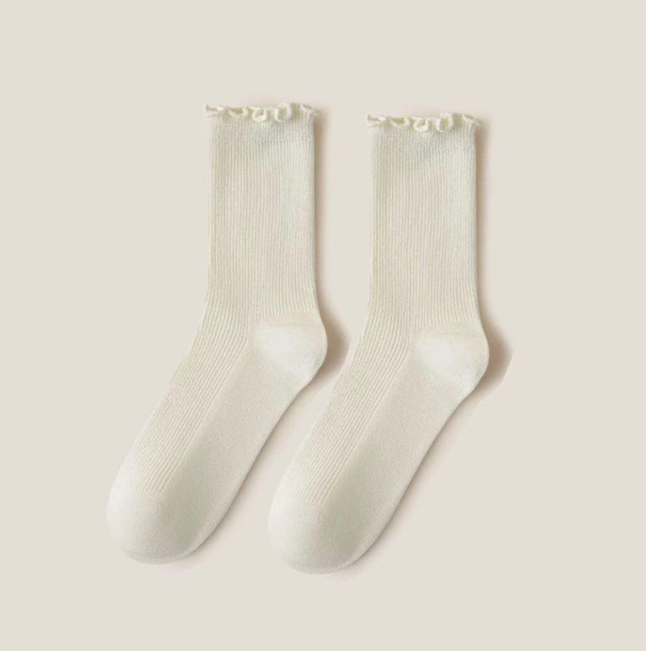 Ruffle crew socks in cream ribbed knit, featuring a frilled ruffle cuff. Shown as a flat-lay pair on a light surface.
