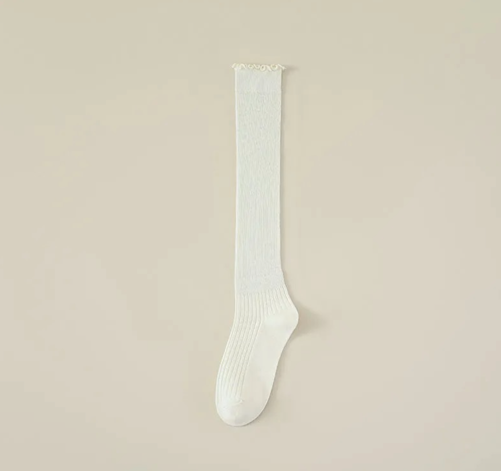 Ruffle knee high socks in white ribbed knit, featuring a frilled ruffle cuff. Shown as a single flat-lay on a neutral backdrop.
