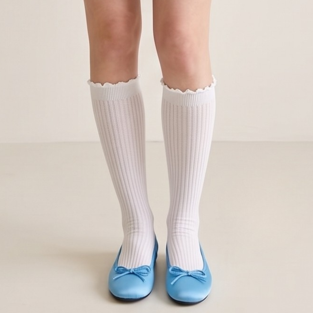 Ruffle knee high socks in white ribbed knit, featuring a scalloped ruffle cuff. Worn on legs with blue ballet flats.