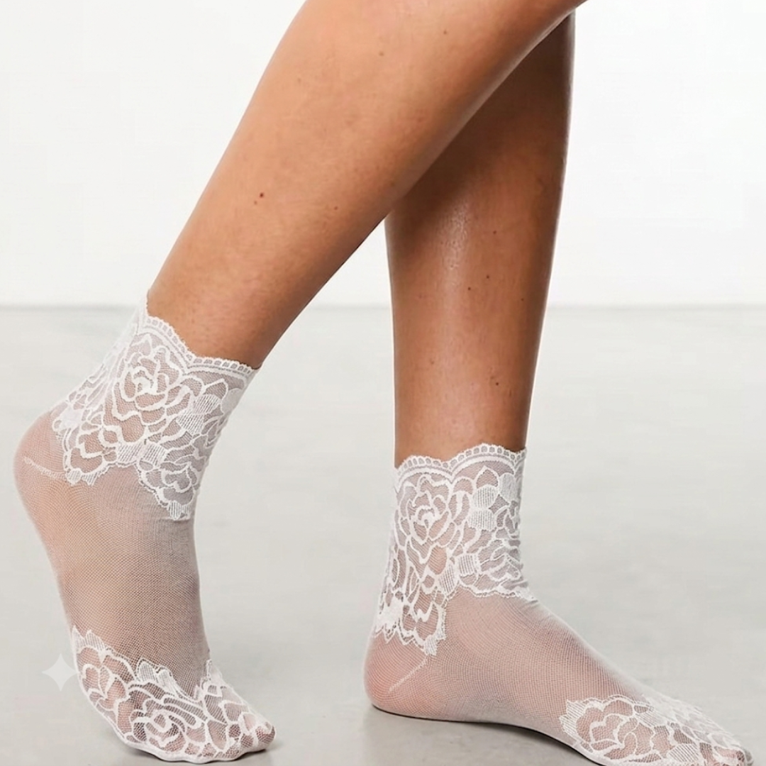 Sheer ankle socks in white floral lace, featuring a delicate mesh pattern. Worn on feet against a soft backdrop.