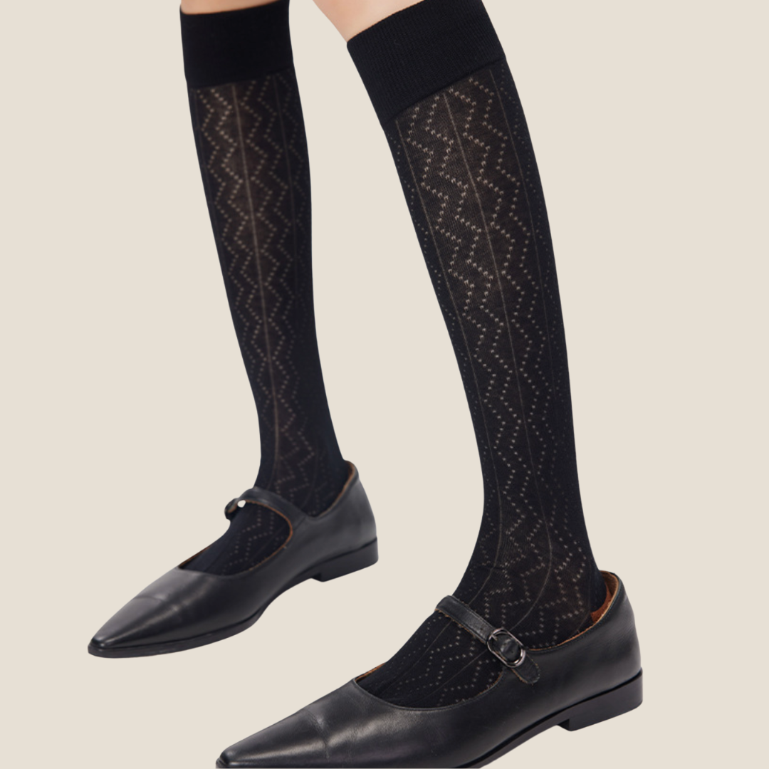 Sheer high knee socks in black sheer knit, featuring a zigzag openwork pattern. Styled on legs with black loafers.