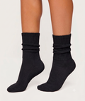 A pair of black ribbed crew socks worn on a model's feet, shown against a plain light gray studio background.