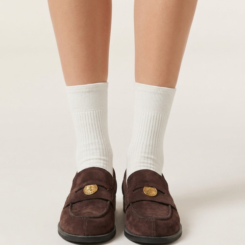 Socks for loafers women in white ribbed cotton, worn with brown penny loafers. Front view of both feet on a plain backdrop.