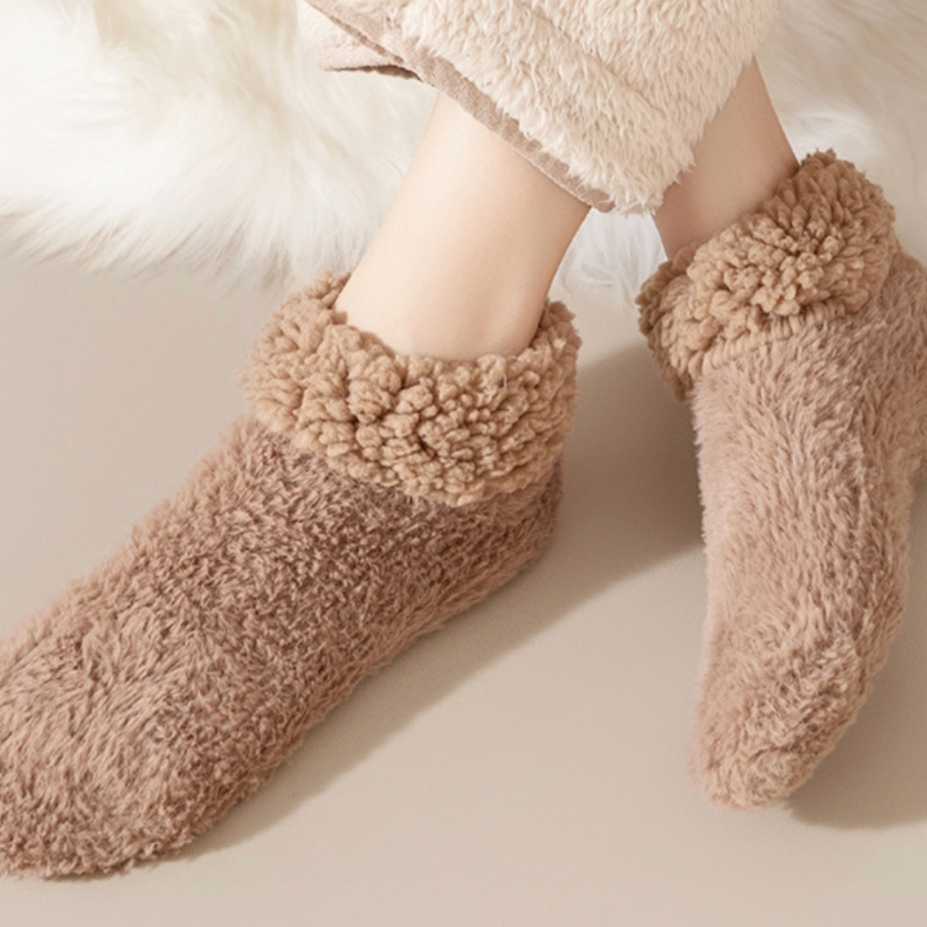 Soft slipper socks in tan plush knit, featuring an ultra-soft fuzzy body. Worn on feet in a cozy setting.