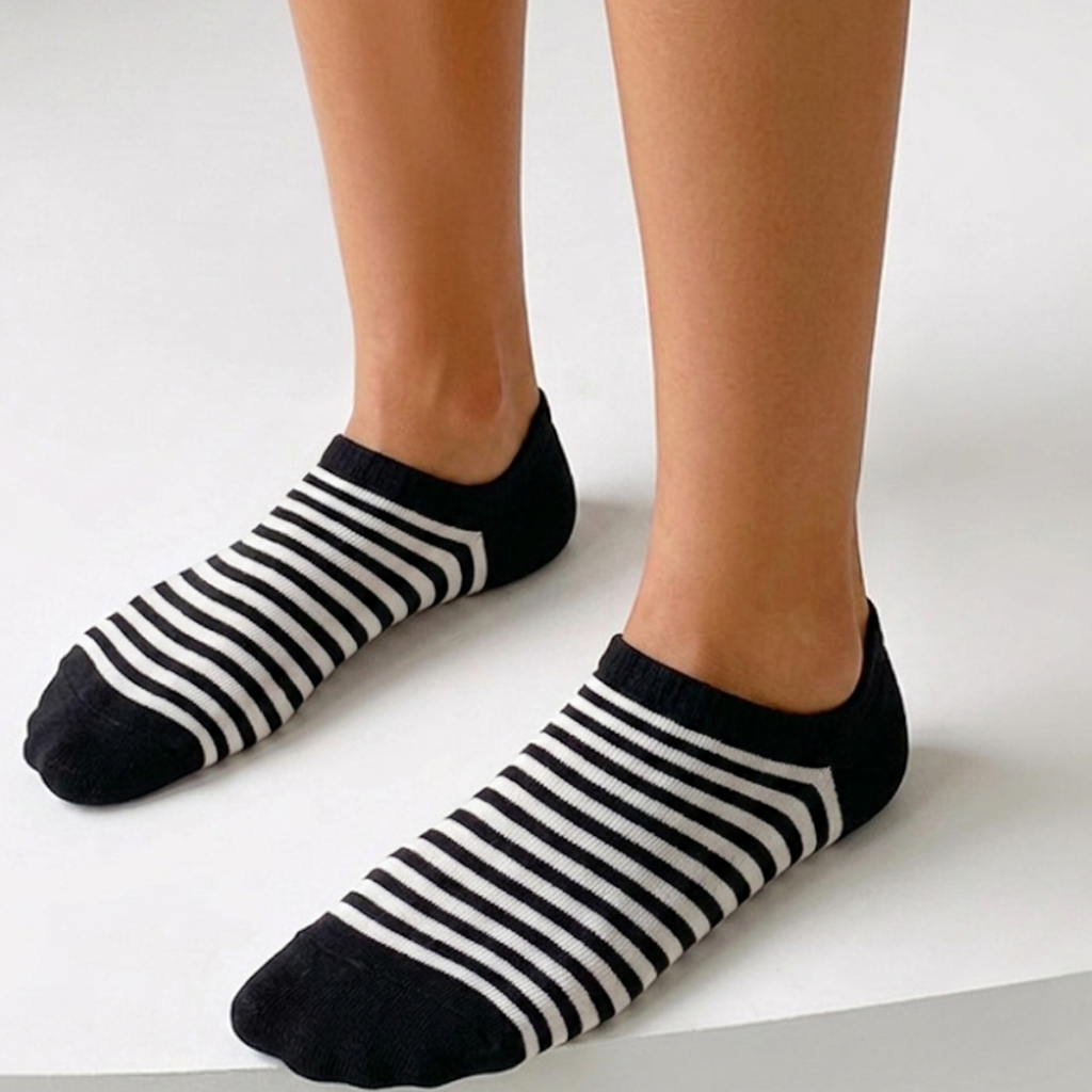 Striped ankle socks in black and white stripes, featuring a retro banded knit. Worn on feet in a bright setting.