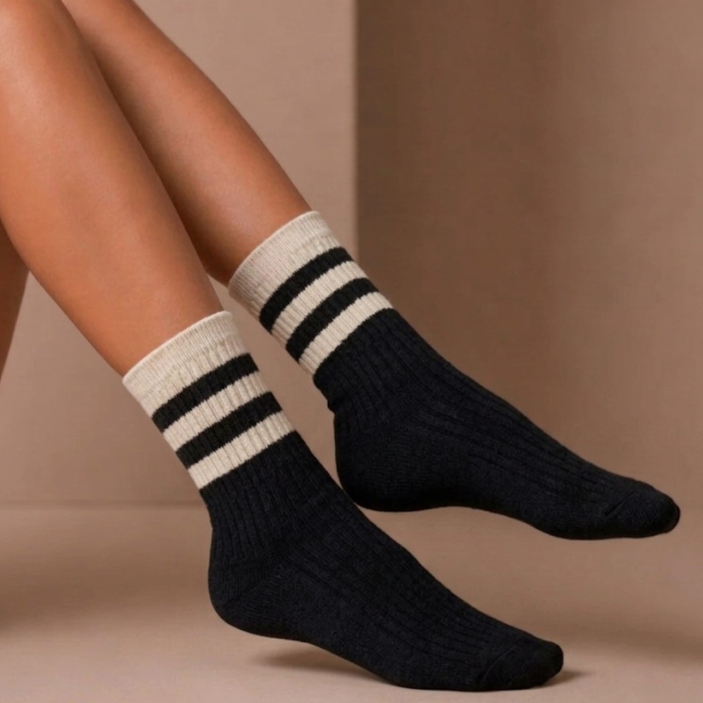 Striped crew socks in black ribbed knit, featuring a cream varsity stripe cuff. Worn on the feet in a casual look.
