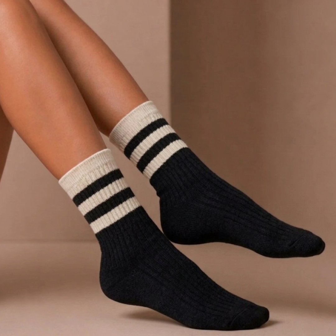 Striped crew socks in black ribbed knit, featuring a cream varsity stripe cuff. Worn on the feet in a casual look.