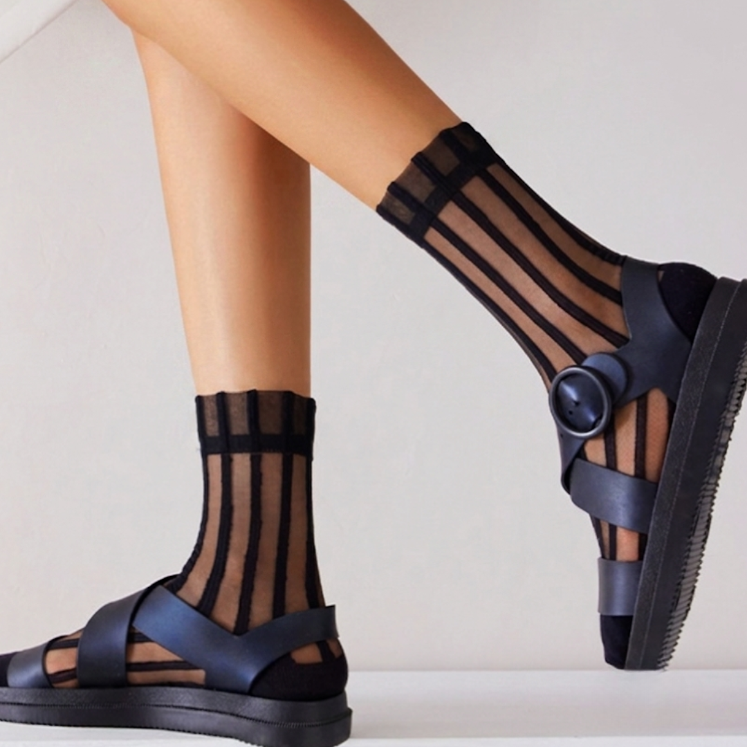 Striped sheer socks in black with sheer stripes, worn on the feet with sandals, side view.