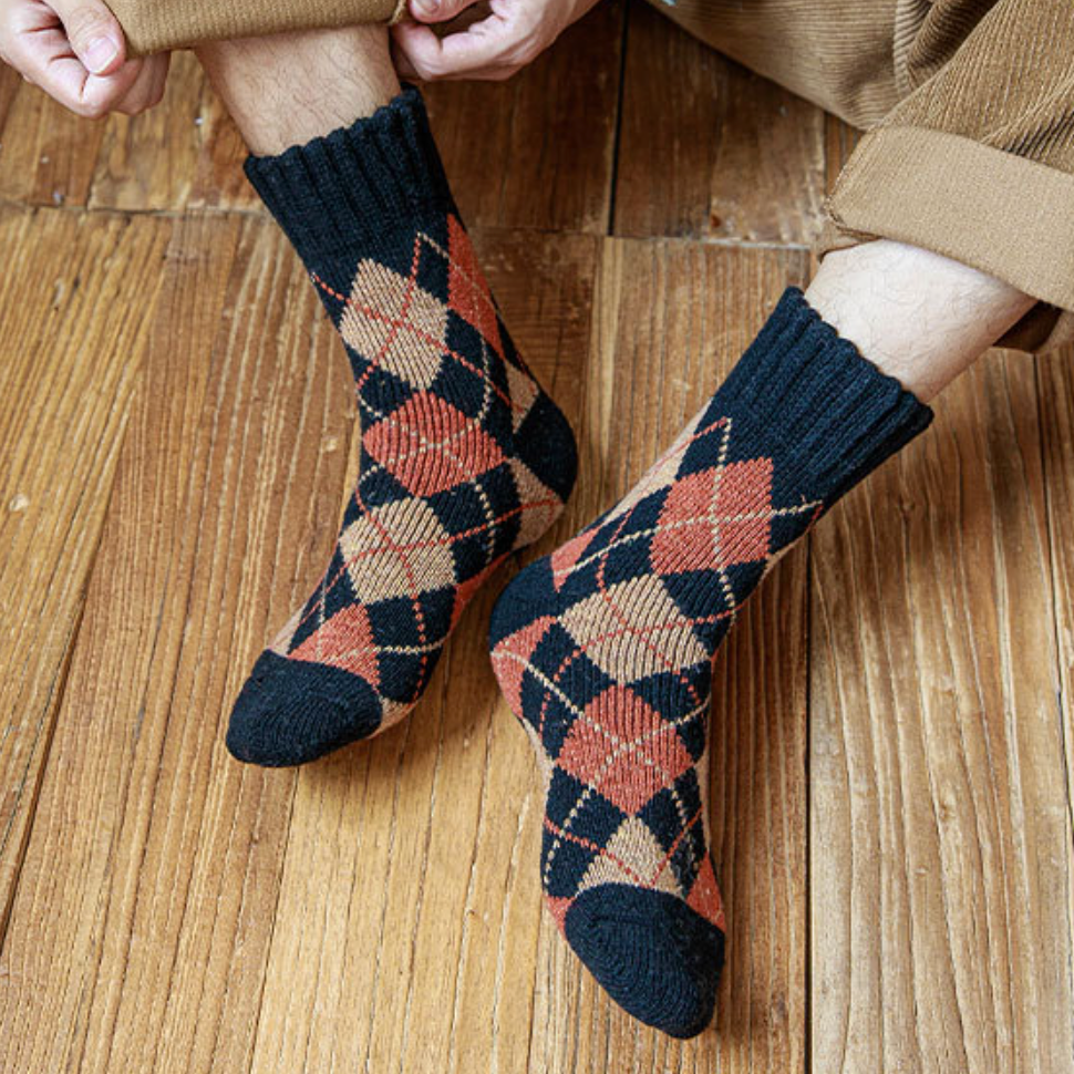 Thermal socks for work in charcoal argyle wool with orange and cream diamonds, worn on the feet on a wood floor.