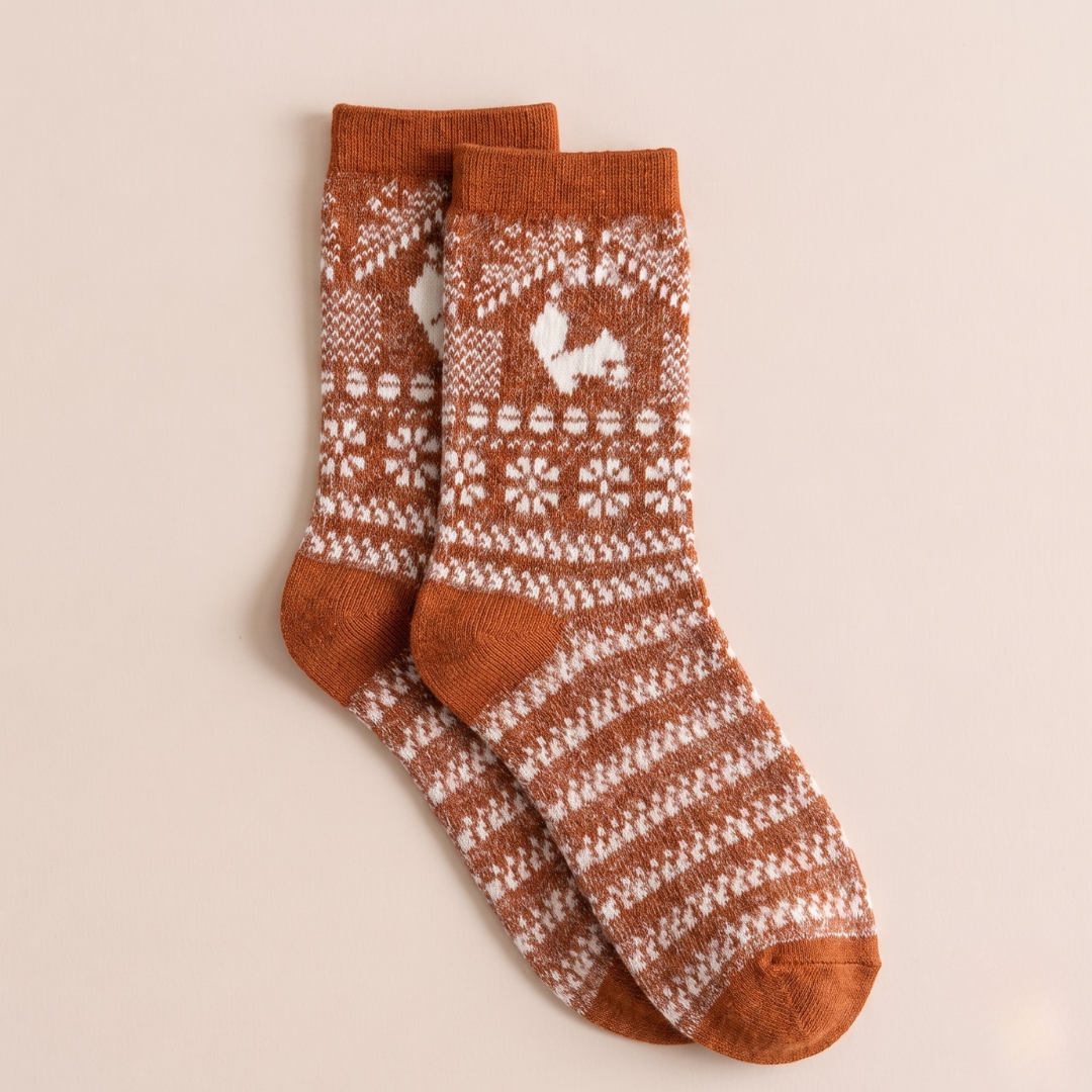 Warm boot socks in rust orange and cream wool, featuring a Nordic reindeer Fair Isle pattern. Shown as a single flat-lay on a neutral backdrop.
