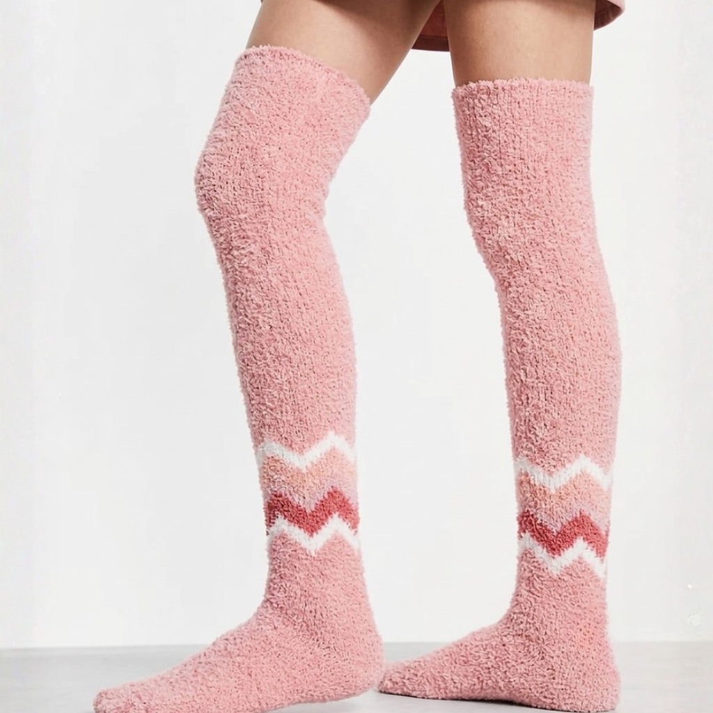 Warm socks for cold feet in pink plush knit, featuring a white and pink chevron stripe. Worn on legs in a cozy indoor setting.