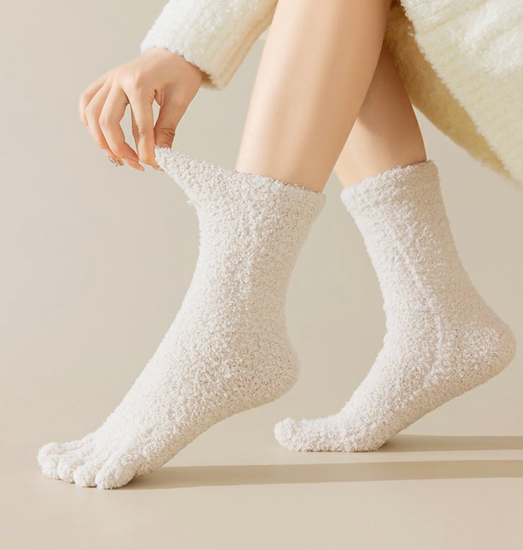 Warm toe socks in cream fuzzy fleece, featuring plush individual toe pockets. Worn on crossed legs in a warm setting.
