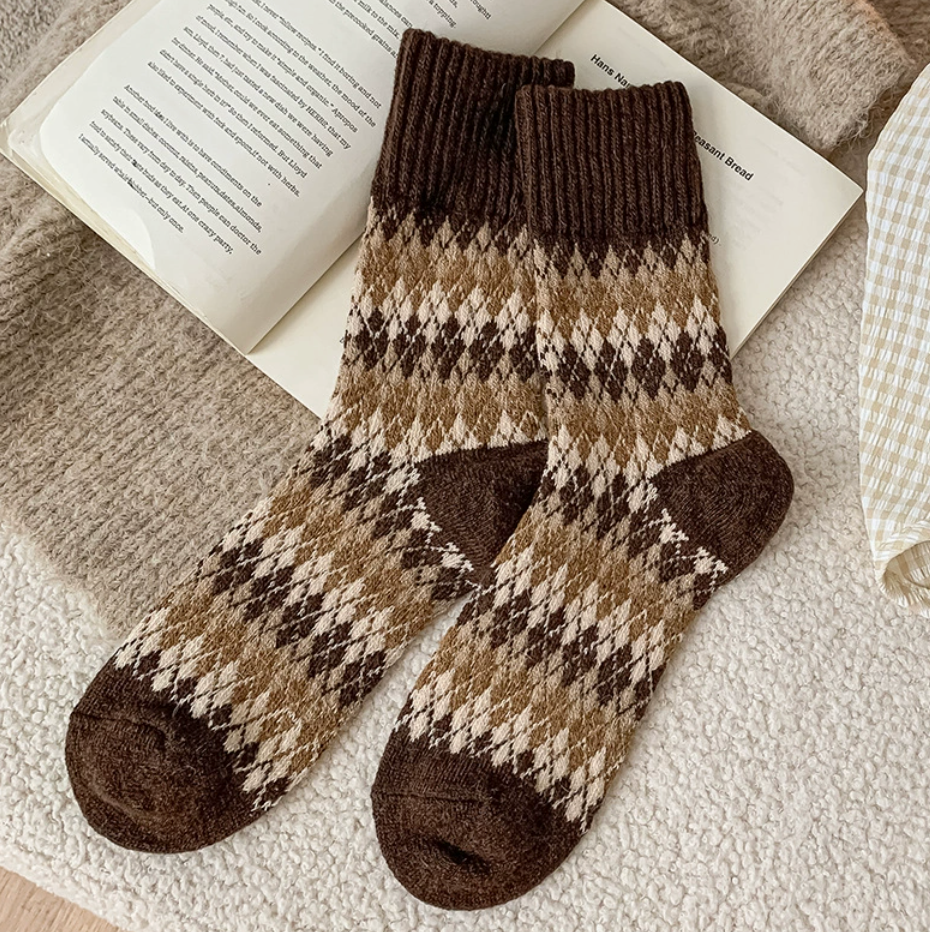 Warm winter socks in warm brown wool, featuring a cream Fair Isle diamond pattern. Displayed flat on a textured knit throw.