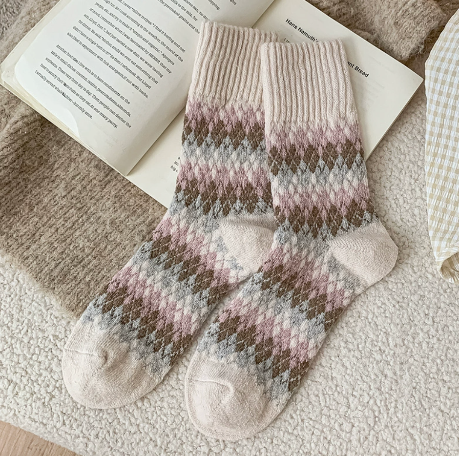 Warm winter socks in cream wool blend, featuring a mauve Fair Isle band. Styled flat on a knit blanket beside an open book.