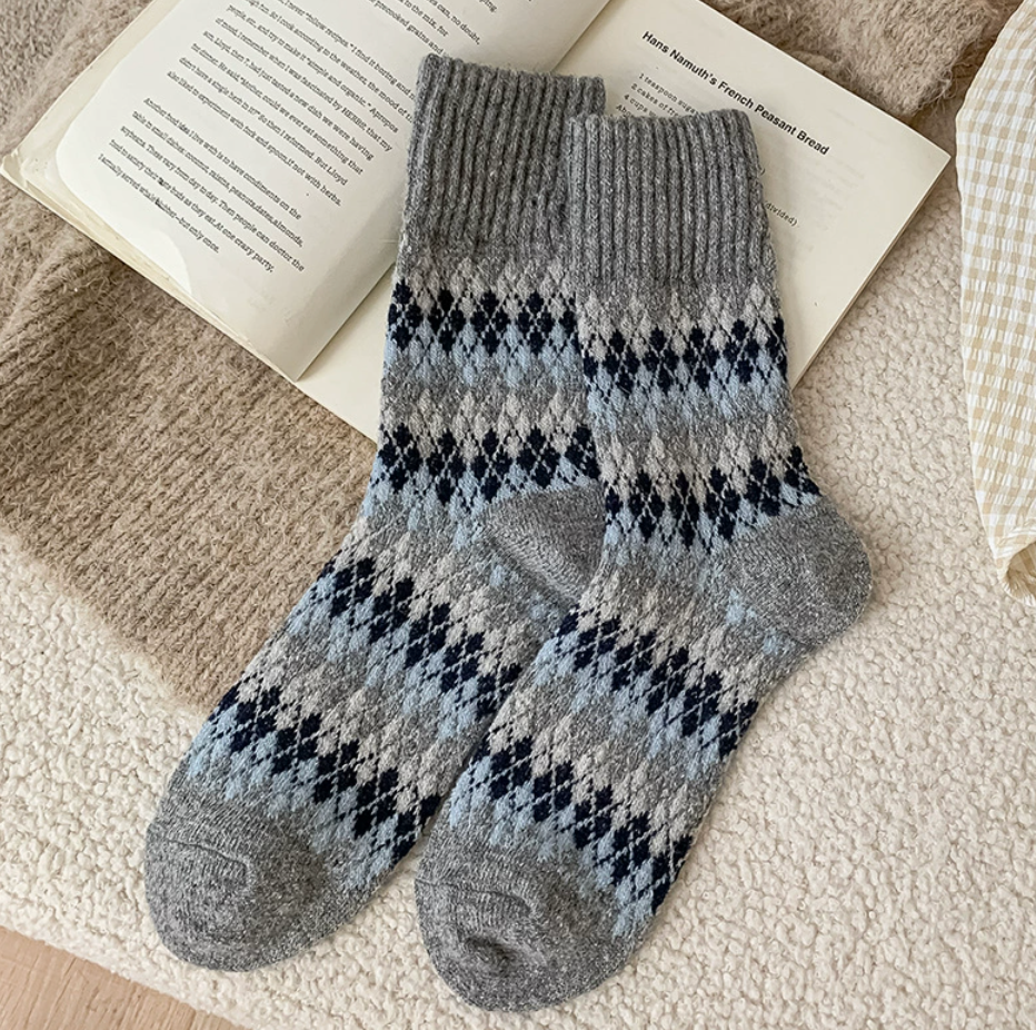 Warm winter socks in heather grey wool, featuring a navy diamond Fair Isle motif. Arranged as a flat-lay pair on a cozy blanket.