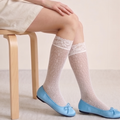 White lace knee high socks in white knit, featuring a lace-trim cuff. Worn with blue bow flats in a seated pose.