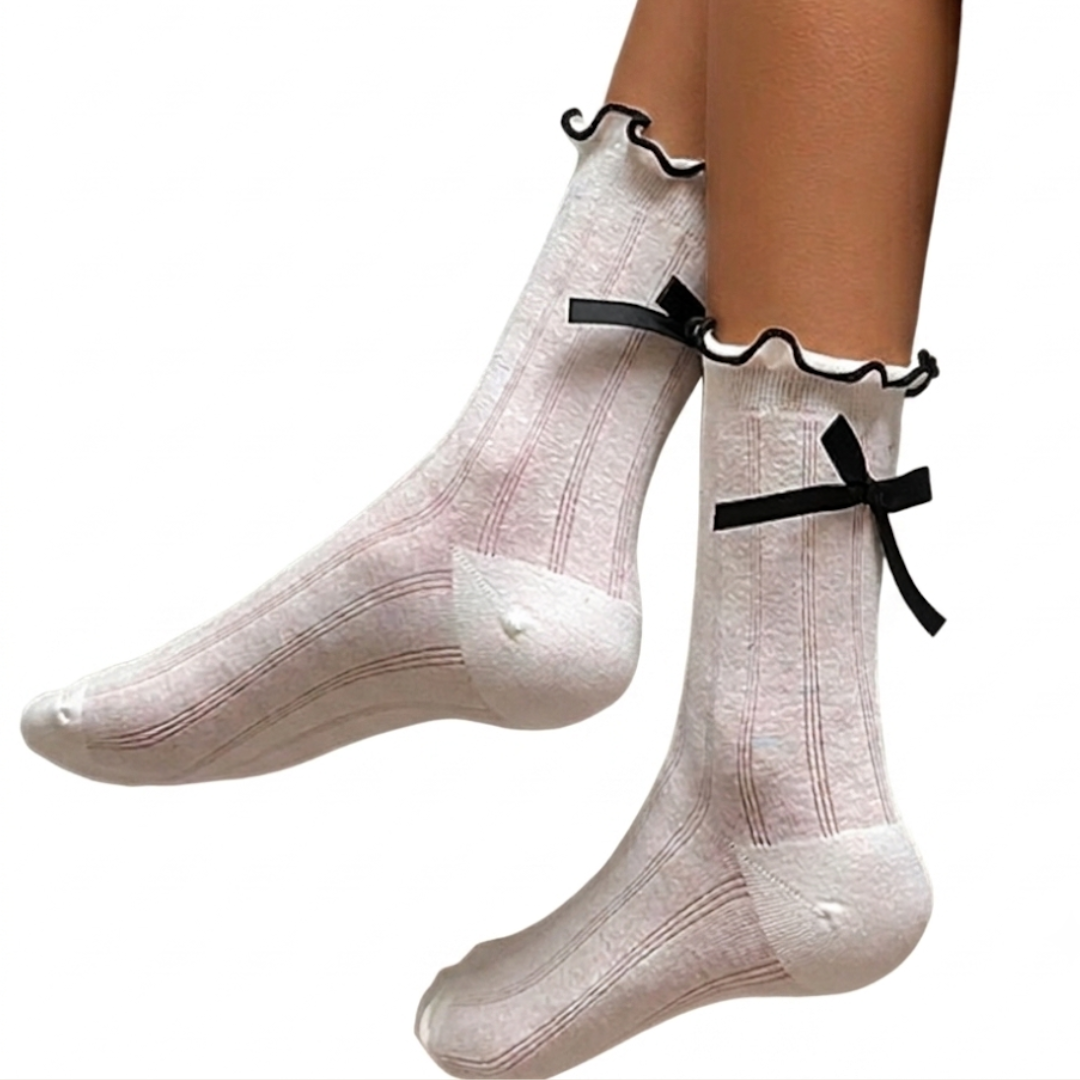 White ruffle socks with a black ruffle trim and back bow, worn on the feet, side view.