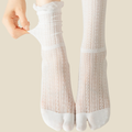 White tabi socks in white, featuring a split-toe ribbed knit. Worn on feet to display the divided toe.