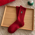 Women's Christmas socks in red with an embroidered holiday motif, single sock styled on a wooden tray.