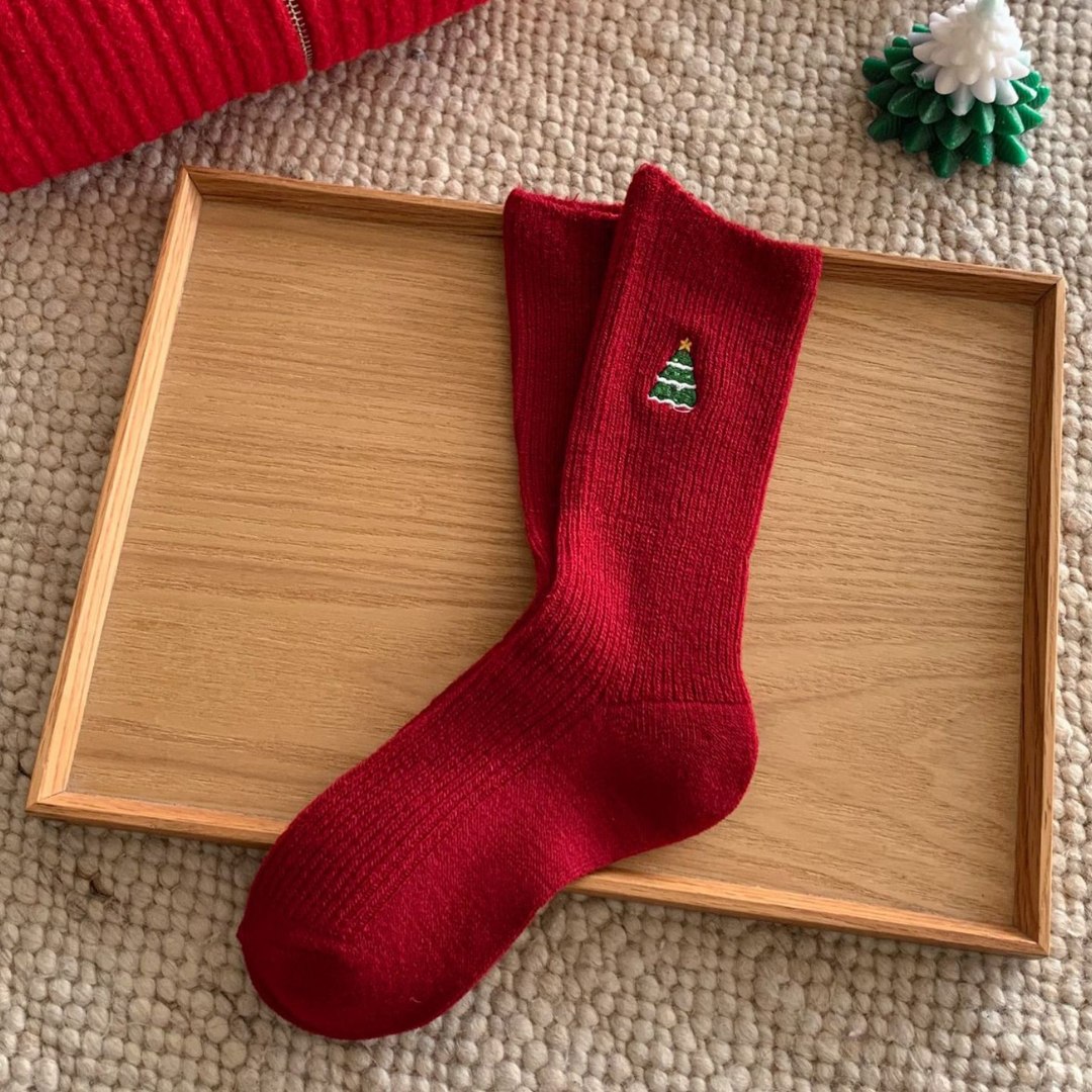 Women's Christmas socks in red with an embroidered holiday motif, single sock styled on a wooden tray.