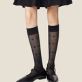 Women's black knee socks in sheer patterned knit, featuring a delicate texture. Worn with a black skirt.