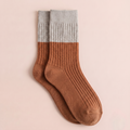 Women's merino wool dress socks in rust brown with a grey cuff, featuring a color-block ribbed knit. Shown as a single flat-lay on a pink backdrop.