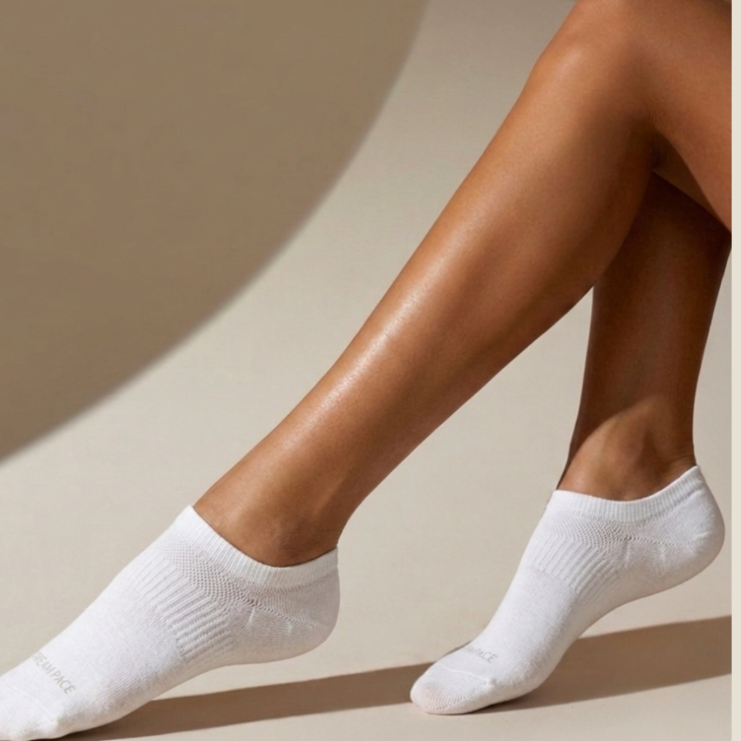 Women's no show socks in white, featuring an invisible low-cut design. Worn on feet in a bright studio setting.