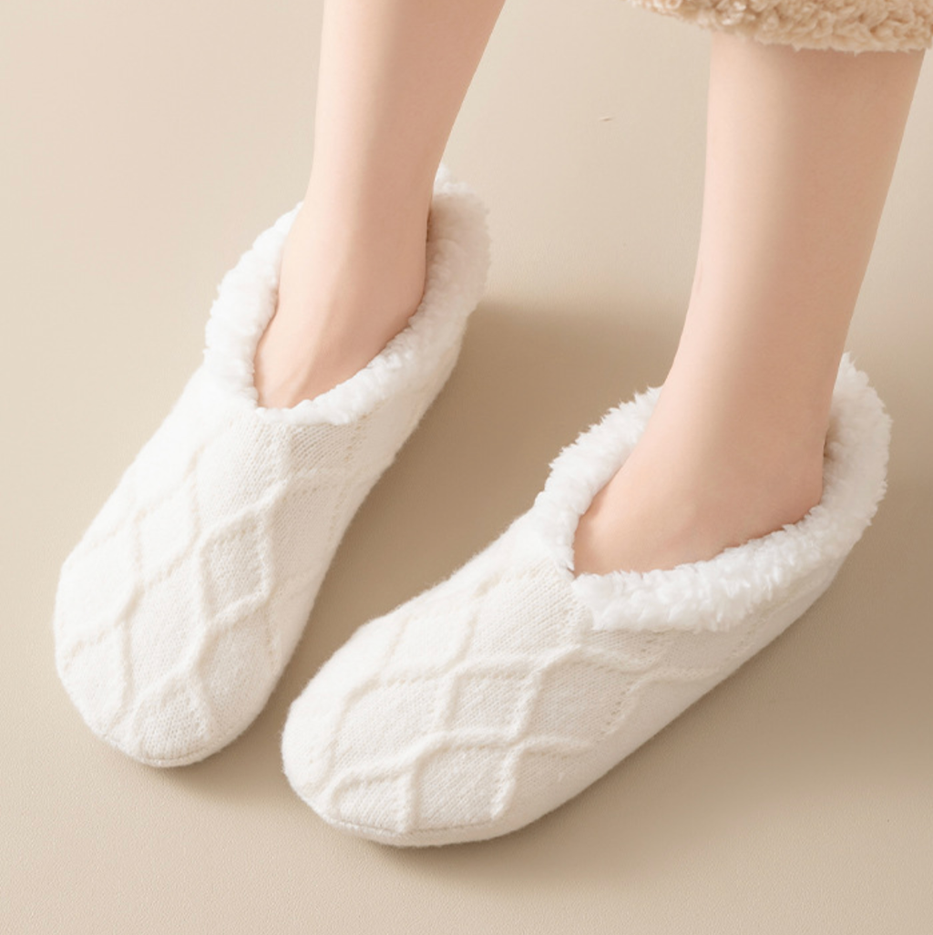 Women's slipper socks in cream, featuring a plush non-slip sole. Worn on feet in a cozy setting.