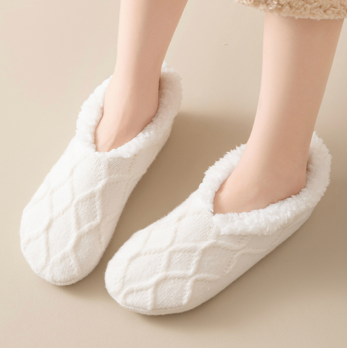 Women's slipper socks in cream, featuring a plush non-slip sole. Worn on feet in a cozy setting.
