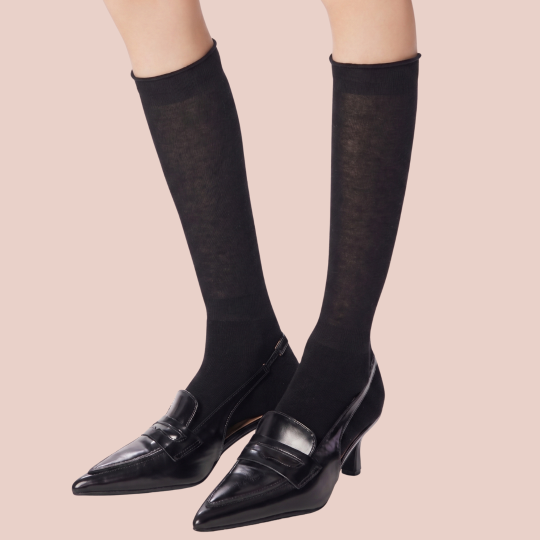 Women's thin wool dress socks in black fine-ribbed wool, featuring a lightweight leg. Worn with black heels.