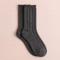 Women's wool dress socks in charcoal cable knit, featuring a ruffled cuff. Shown as a flat-lay pair on a pink backdrop.