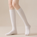 Women's wool knee socks in cream ribbed knit, featuring a snug knee-high fit. Worn on bent legs against a soft backdrop.