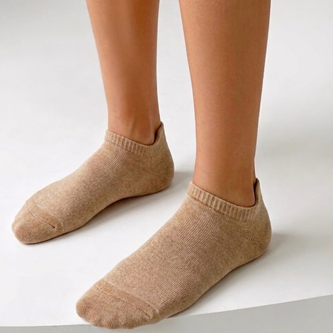 Wool ankle socks in tan, featuring a warm ribbed knit. Worn on feet in a cozy setting.