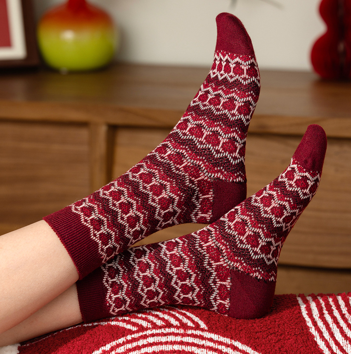 Wool Christmas socks in burgundy Fair Isle knit worn on the legs in a cozy holiday setting.