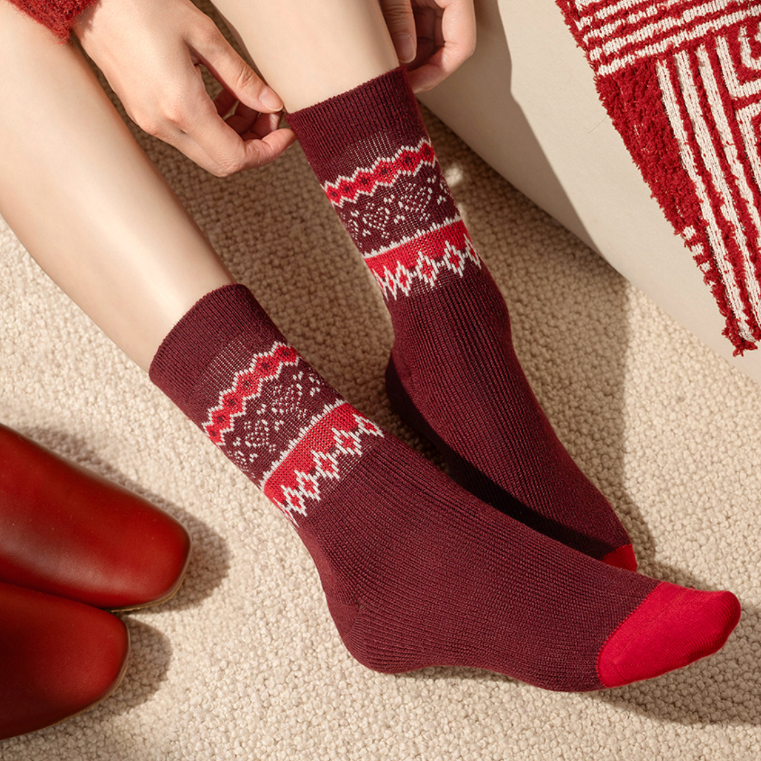 Wool Christmas socks in burgundy merino Fair Isle knit, worn on the feet beside a woven rug, side view.