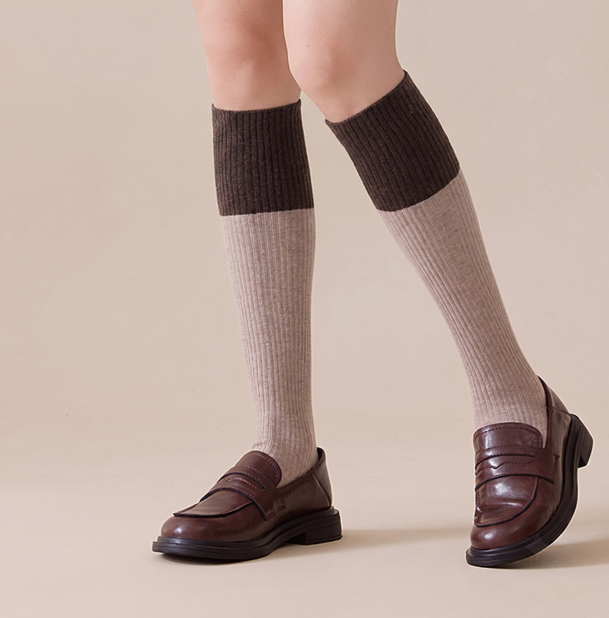 Wool knee socks in oatmeal with a dark brown cuff, featuring a chunky ribbed leg. Worn on feet with brown loafers.