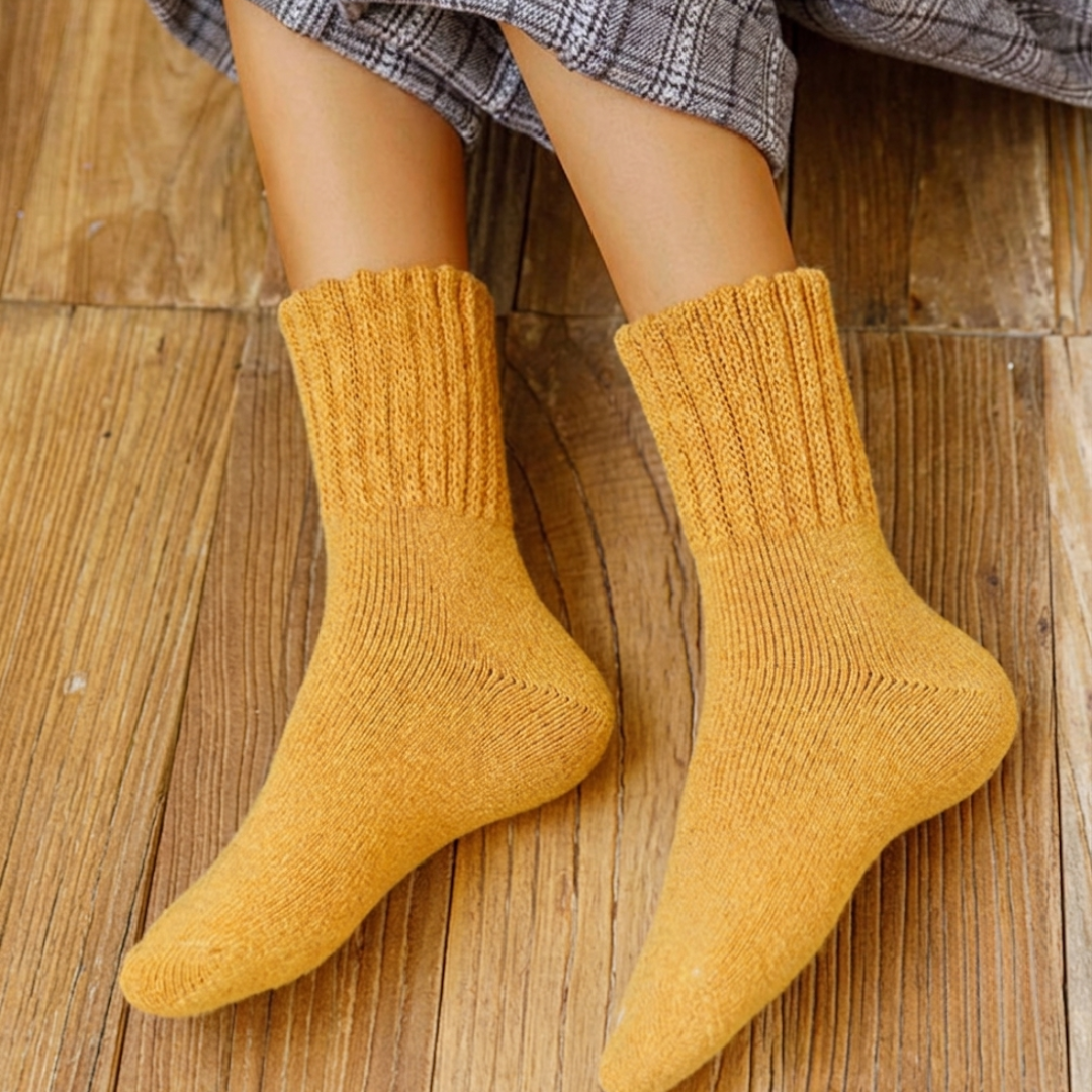 Wool thick socks in mustard yellow, featuring a chunky ribbed knit. Worn on feet on a wooden floor.