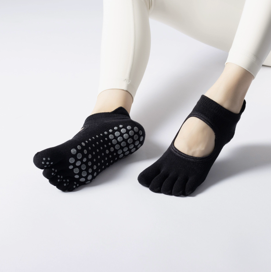 Yoga toe socks in black knit, featuring an open-toe backless design with grip sole. Worn during a yoga pose.