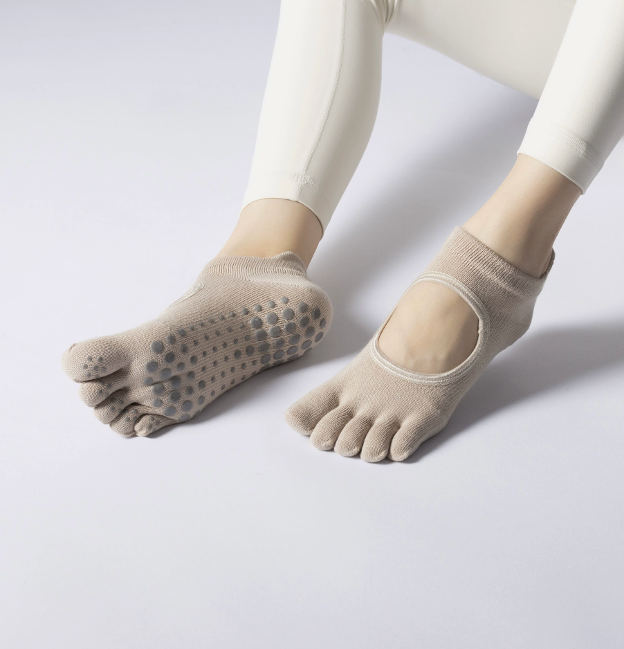 Yoga toe socks in tan knit, featuring a five-toe open design with non-slip sole. Worn on the feet from an angled view.